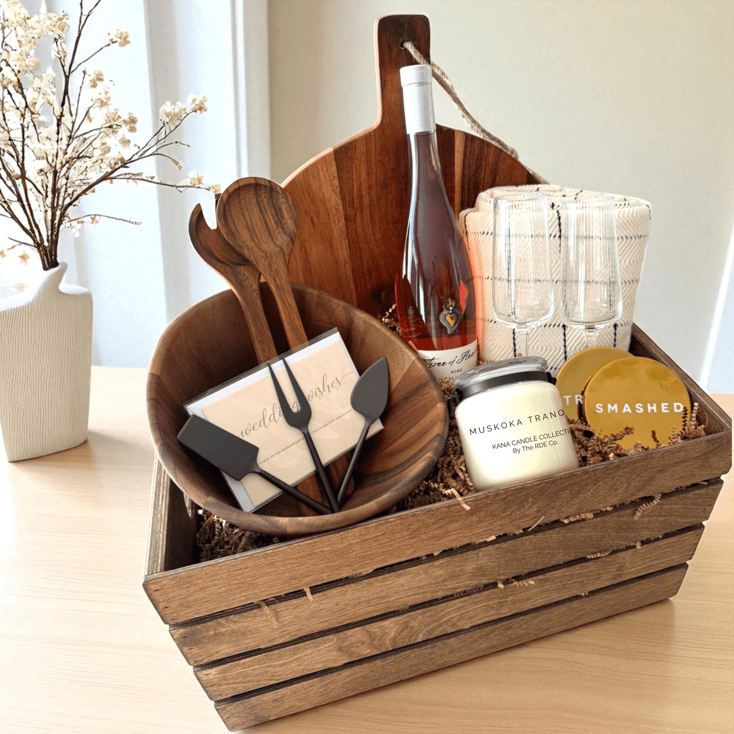 Rustic Luxe 20-inch gift crate with personalized acacia salad bowl and utensils, large farmhouse board, metal cheese knife set, custom Kana candle, cozy throw blanket, wine bottle, and sassy engraved coasters by The RDE Co.