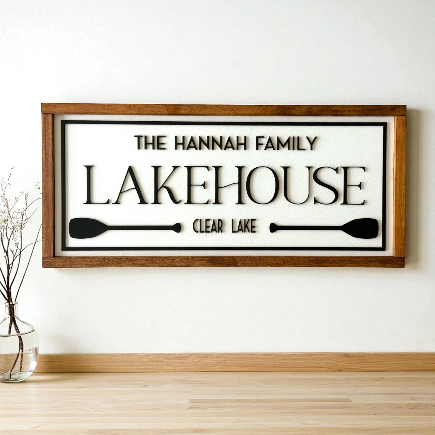 Wooden sign with 'The Hannah Family Lakehouse Clear Lake' text on a white wall.