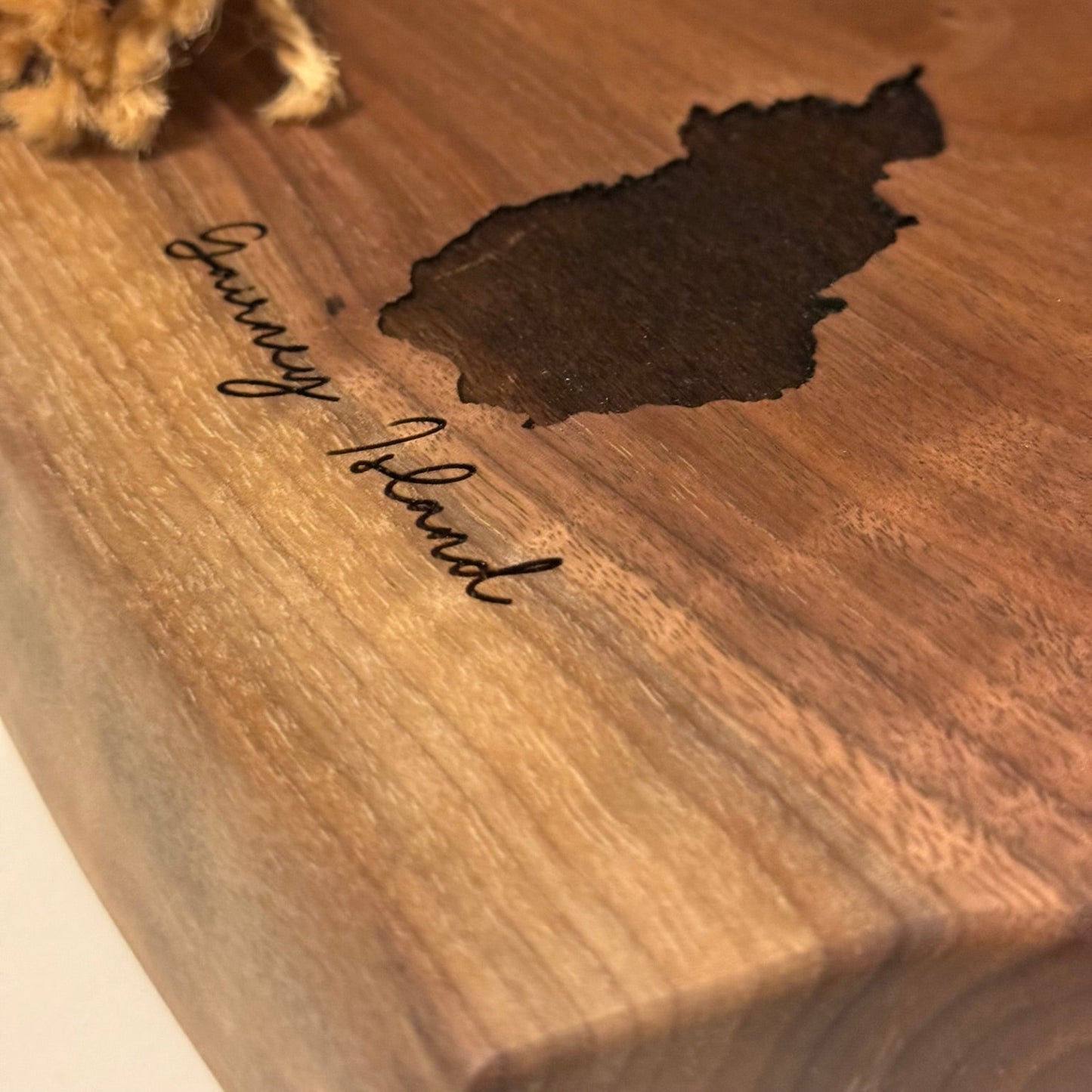 Wooden cutting board with engraved text and and island shape on a wooden surface.