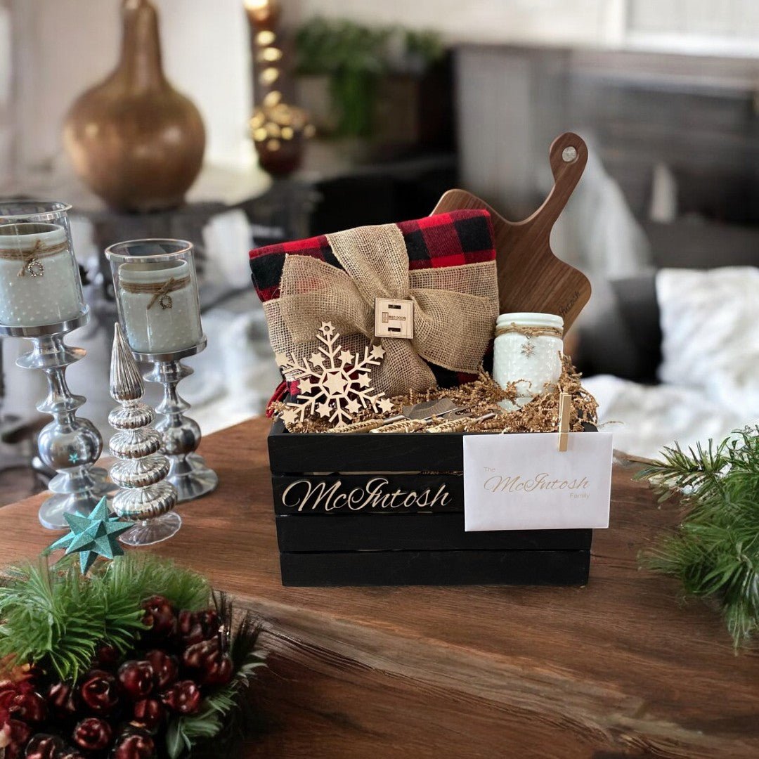 Stained ebony crate filled with acacia cheese board white hobnail candle Christmas check blanket rattan cheese knives and a Baltic birch snowflake ornament