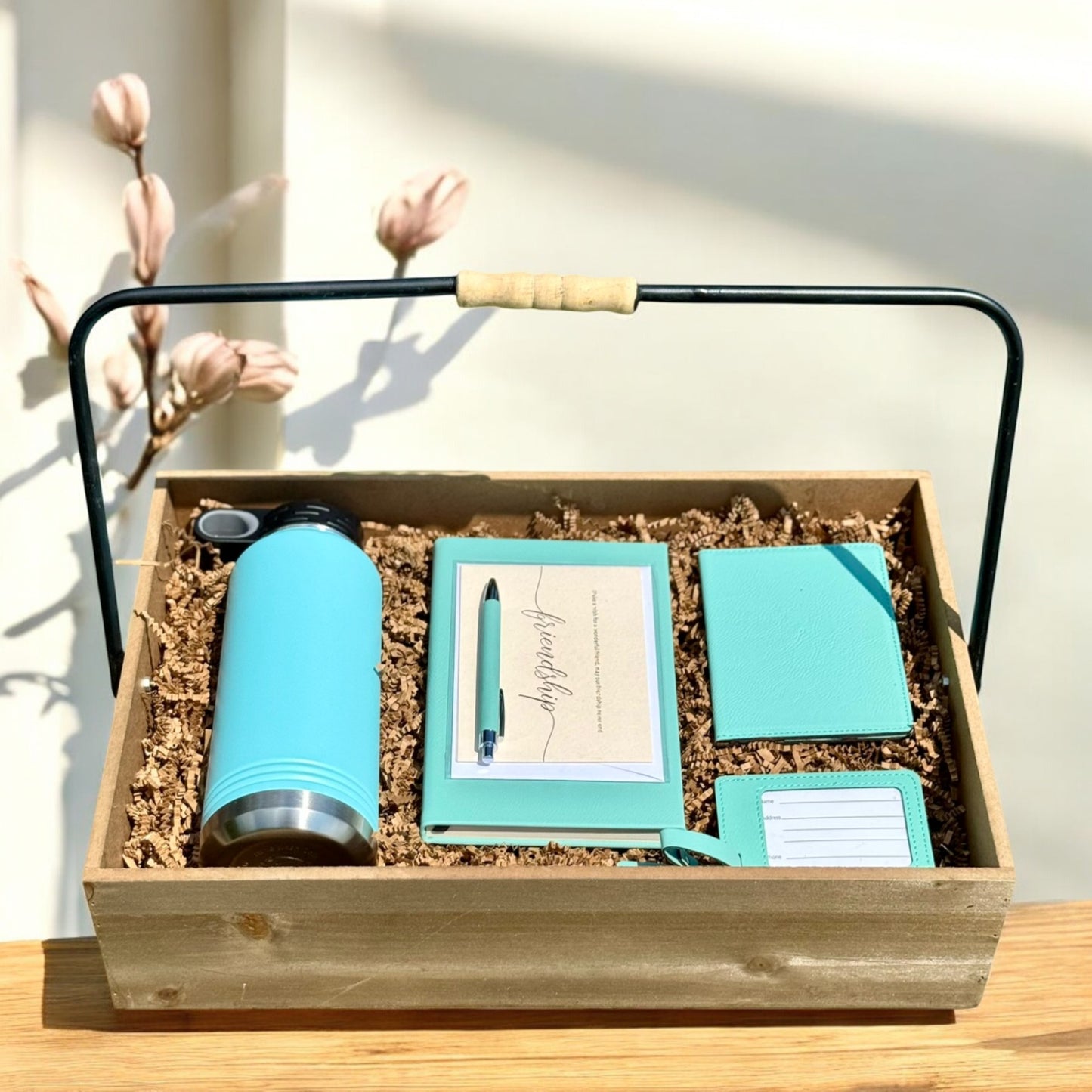 Gift set with teal tumbler, notebook, passport holder, greeting card, luggage tag, and pen in a wooden box.