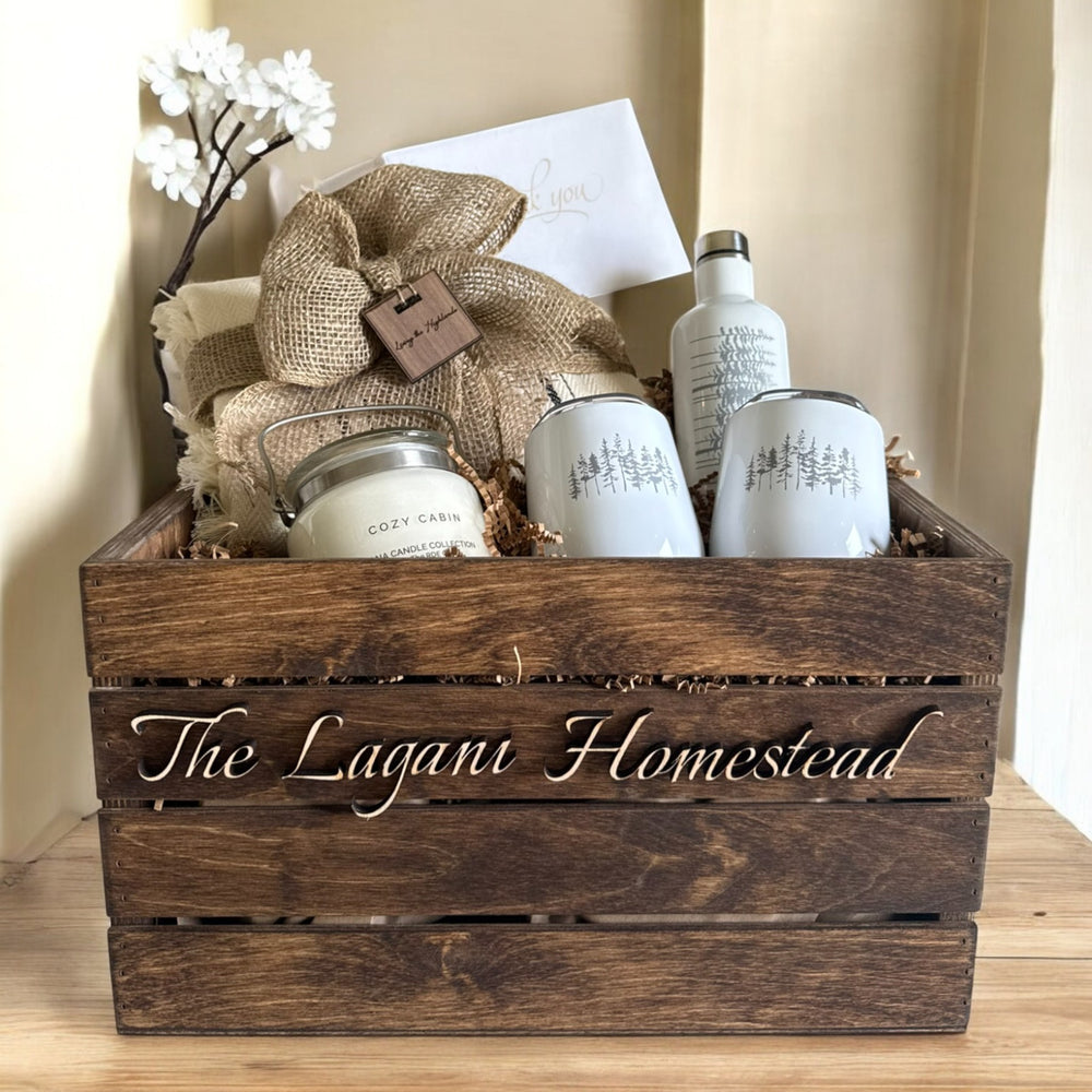 
                  
                    Wooden crate labeled 'The Lagani Homestead' with decorative items including a tumbler bottle, and mugs, a blanket and a candle
                  
                