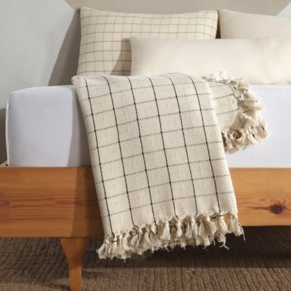 
                  
                    Turkish Throw Blankets in Ivory & Ebony Plaid with tassels neatly folded at the end of  a bed with marching pullows behind 
                  
                