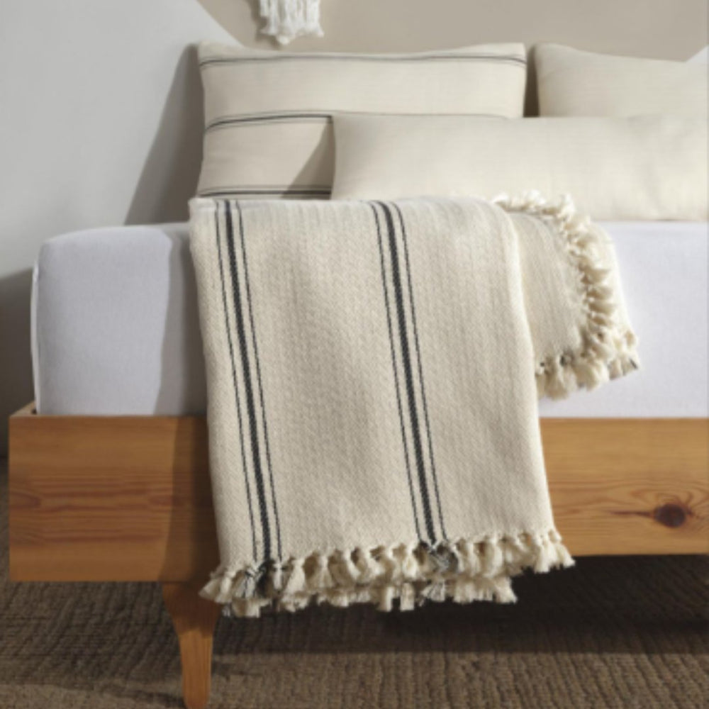 
                  
                    ivory ad ebony throw blanket with tassels folded neatly at the end of a bed with matching pillows behind.
                  
                