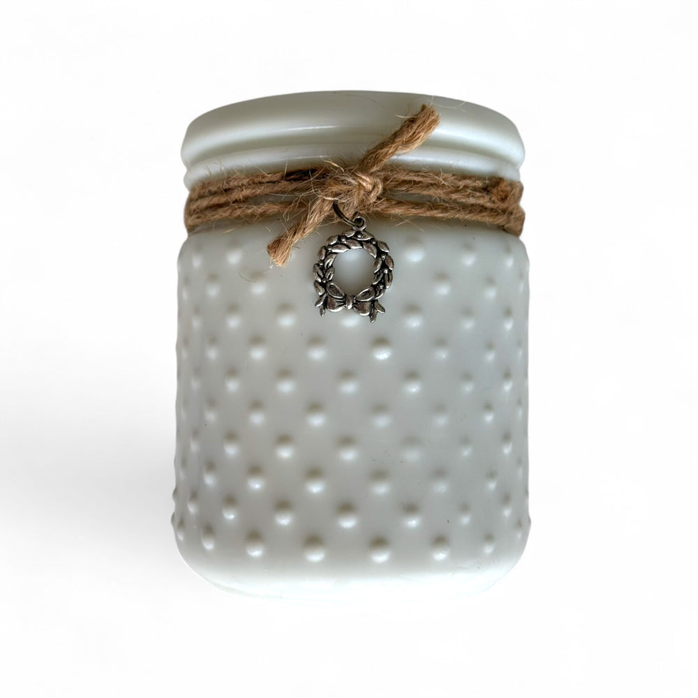 
                  
                    Decorative hobnail candle with milk-white polka-dot textured surface and string bow with Christmas charm on a white background
                  
                