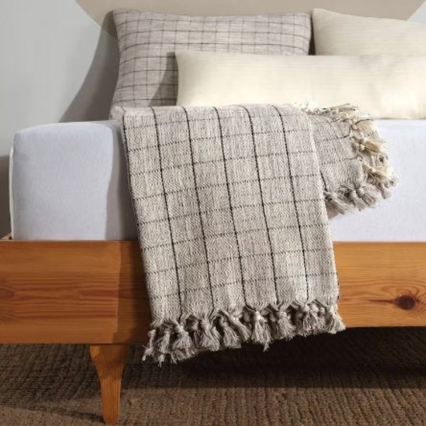 grey and ebony plaid blanket  with tassels hanging neartly over a bed with matching pillows in the back